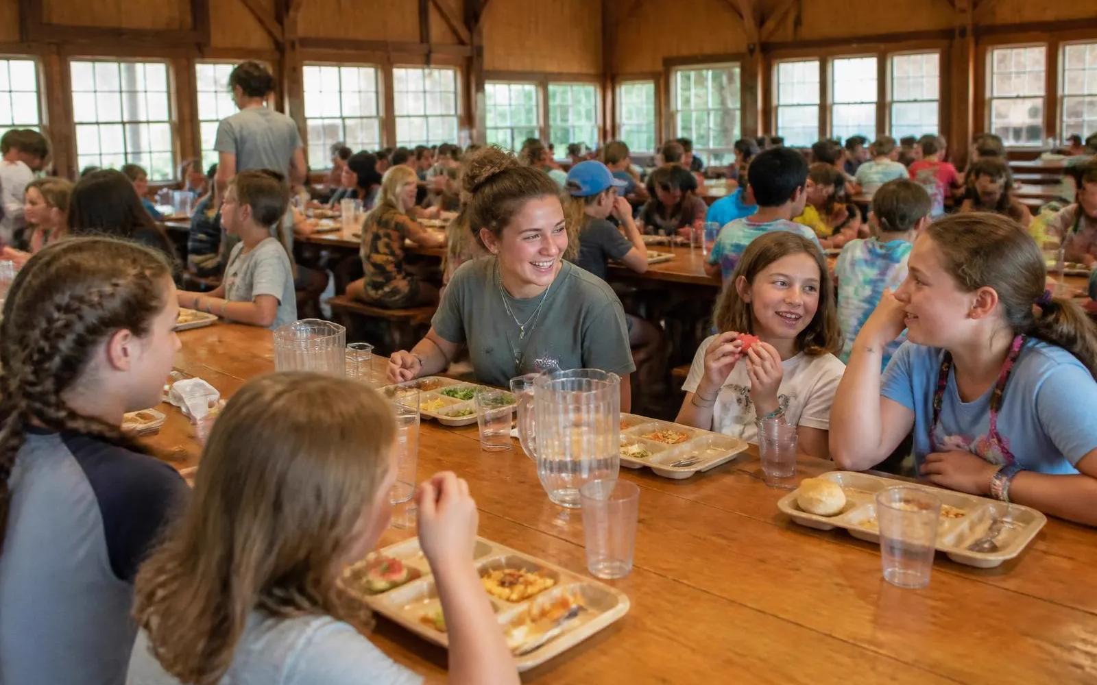 Campers and counselors eating together at long wooden tables in a camp dining hall